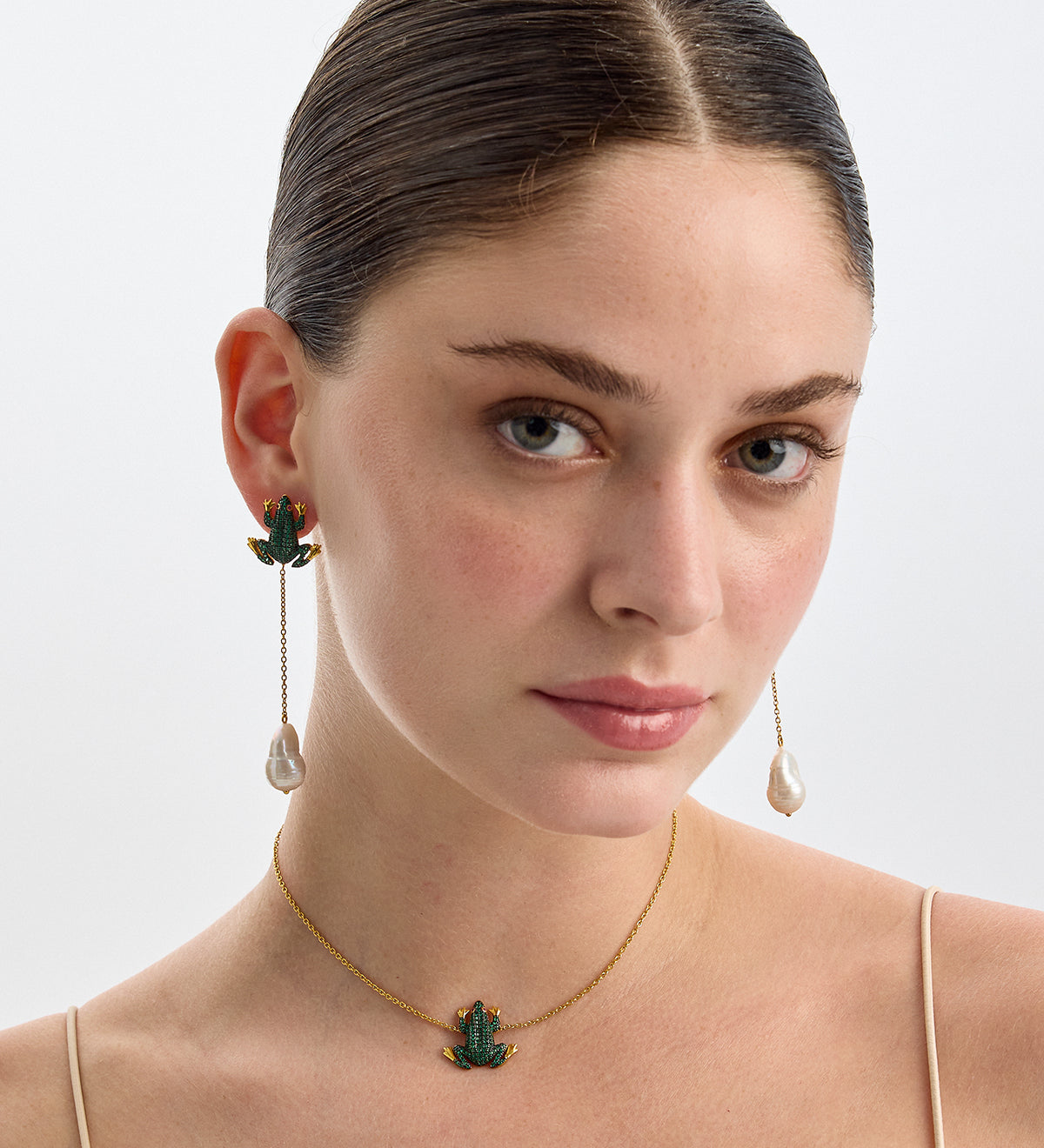 Model wearing a BEGÜM KHAN gold chain necklace with a green leaf pendant and gold earrings with pearl drops